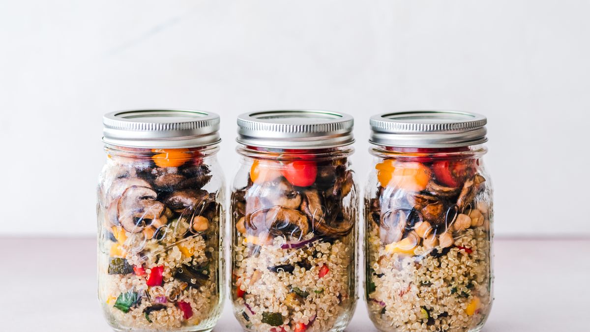 Three lidded glass jars of quinoa salad with mushrooms, peppers, and tomatoes